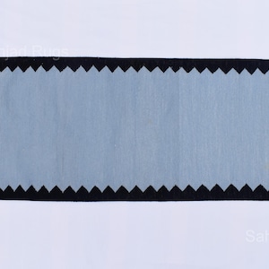 May include: Rectangular rug with a light blue center and a black zigzag border. The rug has a cream-colored fringe on the short ends. The rug is displayed on a white background. The rug is a home decor item.
