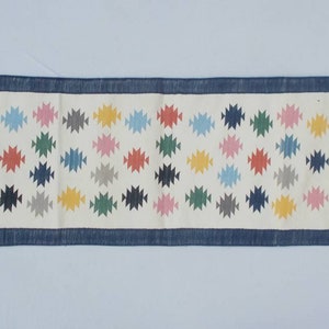 May include: A white runner rug with a blue border and a repeating pattern of colorful geometric shapes.