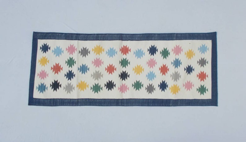 May include: A white runner rug with a blue border and a repeating pattern of colorful geometric shapes.