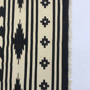 May include: Black and white striped rug with geometric patterns. The rug has a fringe border.