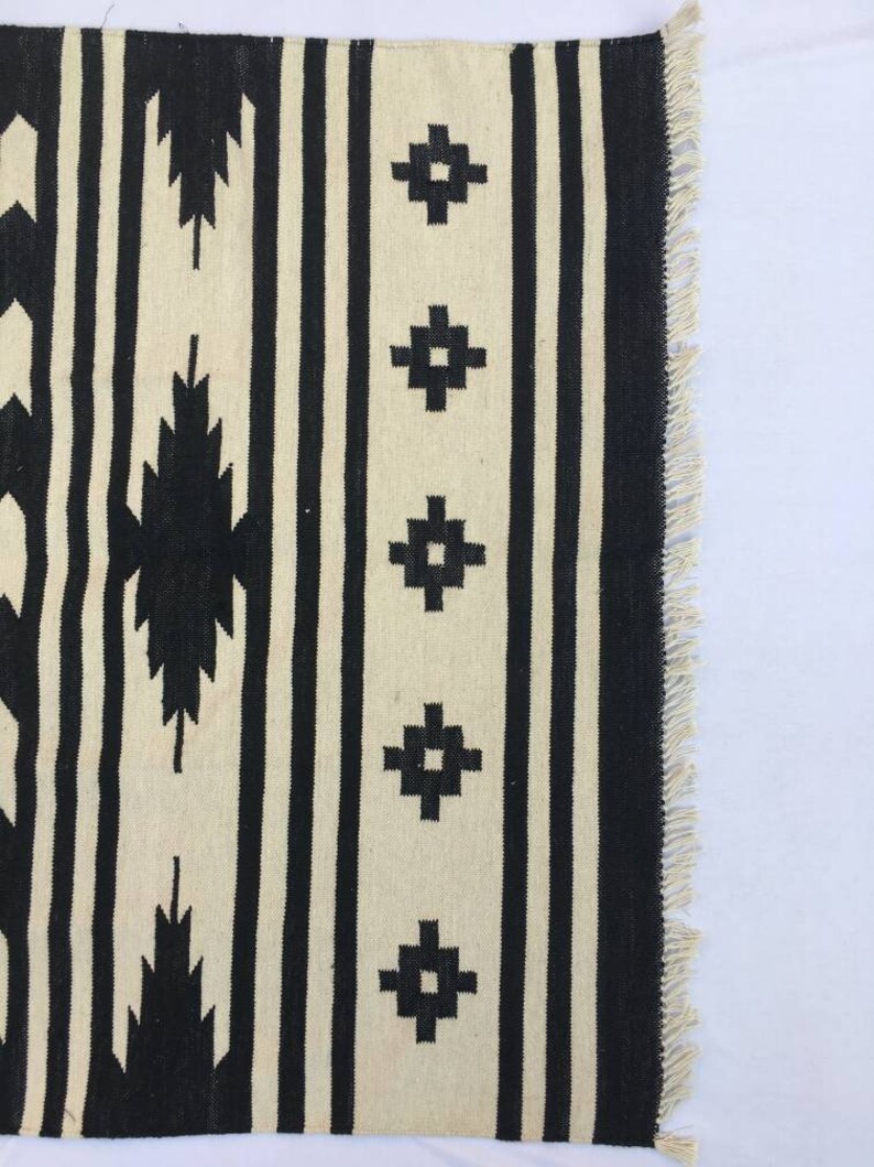May include: Black and white striped rug with geometric patterns. The rug has a fringe border.