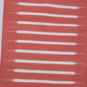 May include: A coral-colored rug with white horizontal stripes. The stripes are woven into the rug and have a slightly frayed edge.