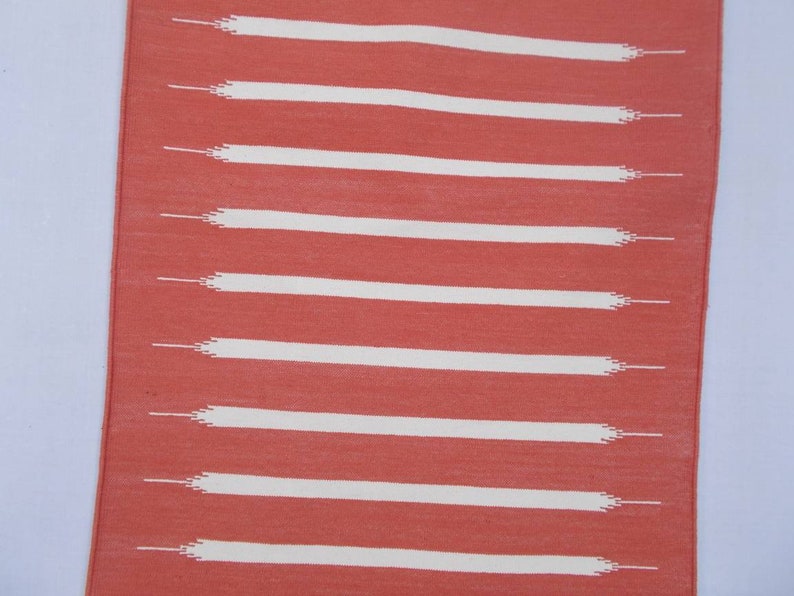 May include: A coral-colored rug with white horizontal stripes. The stripes are woven into the rug and have a slightly frayed edge.