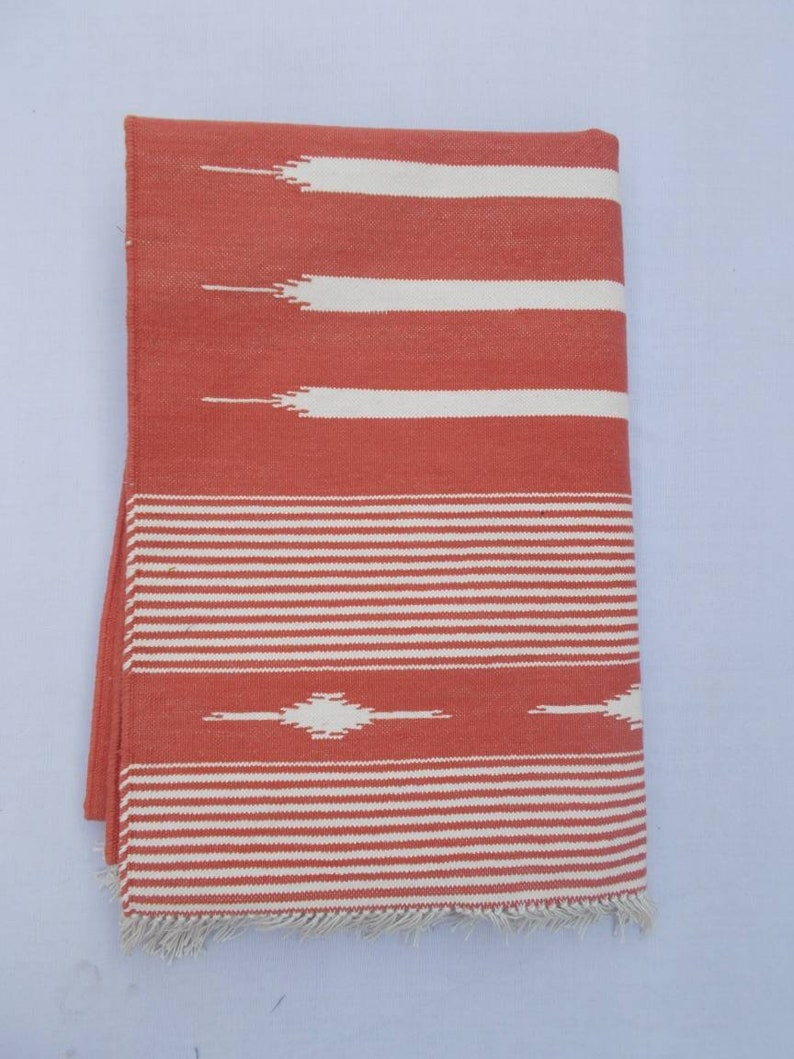 May include: A red and white striped throw blanket with a fringe border. The blanket has a geometric pattern in the center.