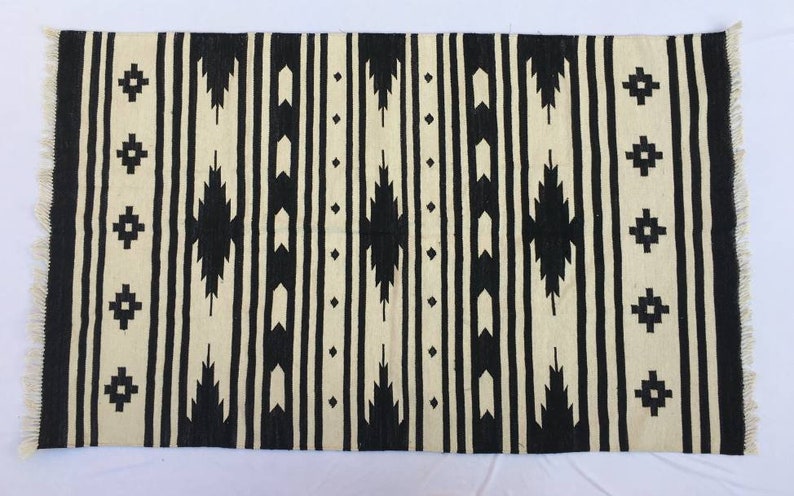 May include: Black and white geometric patterned rug with fringe on the edges. The rug has a traditional design with repeating patterns.