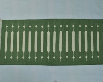May include: A green and white runner rug with a geometric pattern. The rug has a fringe on both ends.