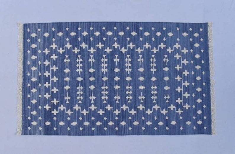 Puede incluir: Una alfombra azul y blanca con un dise&ntilde;o geom&eacute;trico. La alfombra tiene un borde con flecos.