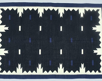 May include: A black and white rug with a geometric pattern. The rug has a blue border and a white fringe.