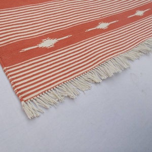 May include: A close-up of a red and white striped rug with a white fringe. The rug has a geometric pattern in the center.
