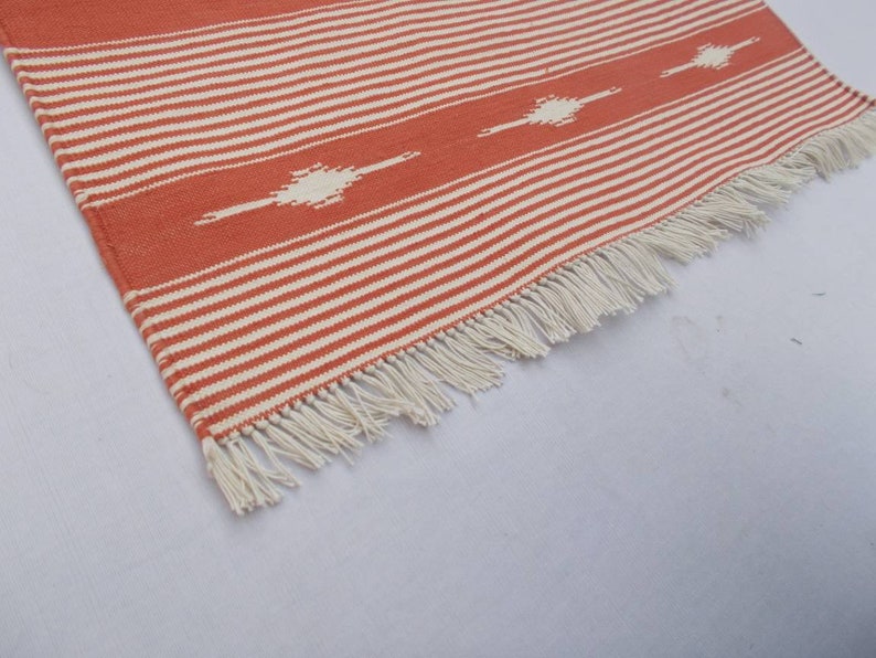May include: A close-up of a red and white striped rug with a white fringe. The rug has a geometric pattern in the center.