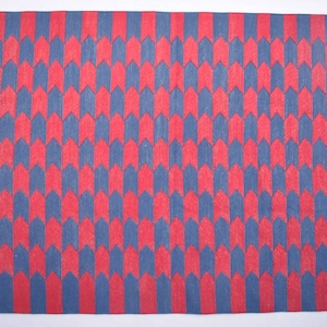 May include: A red and blue geometric patterned rug with a white fringe. The rug has a repeating pattern of arrows pointing upwards.