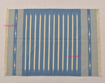 Puede incluir: Alfombra rectangular azul con rayas verticales crema y bordes con flecos. La alfombra presenta un patrón repetitivo de formas de diamante crema a los lados. Adecuada para uso en interiores. Medidas en centímetros.