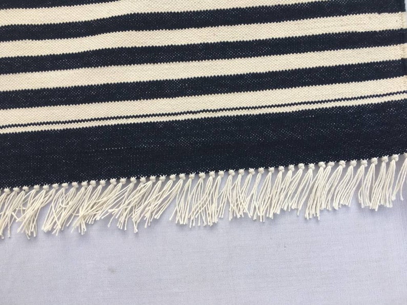 May include: A black and white striped rug with a white fringe. The rug is made of a woven material and has a simple design.