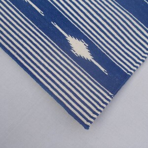 Peut inclure: Gros plan sur un tissu ray&eacute; bleu et blanc avec un motif ikat blanc. Le tissu a une texture tiss&eacute;e et un bord l&eacute;g&egrave;rement effiloch&eacute;.