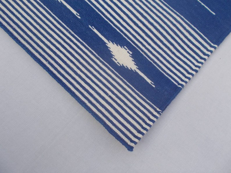 Peut inclure: Gros plan sur un tissu ray&eacute; bleu et blanc avec un motif ikat blanc. Le tissu a une texture tiss&eacute;e et un bord l&eacute;g&egrave;rement effiloch&eacute;.
