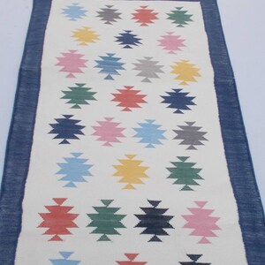 May include: A white runner rug with a blue border and a geometric pattern of colorful stars. The stars are in shades of blue, green, red, pink, yellow, and gray.