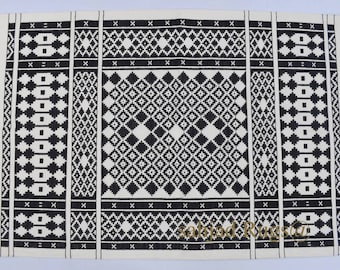 Puede incluir: Alfombra geométrica en blanco y negro con borde de flecos. La alfombra tiene un patrón central de diamante rodeado por un borde de patrones de diamante más pequeños.