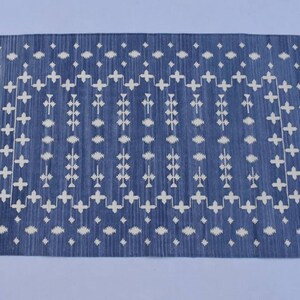 Puede incluir: Una alfombra tejida azul y blanca con un patr&oacute;n geom&eacute;trico. La alfombra tiene un borde de flecos.