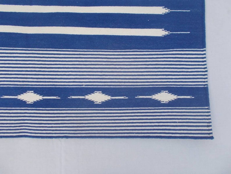 Peut inclure: Tapis ray&eacute; bleu et blanc avec un motif en losange. Le tapis a une texture tiss&eacute;e et une bordure frang&eacute;e.