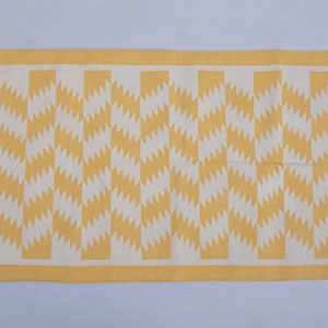May include: A yellow and white geometric patterned rug with fringed edges.