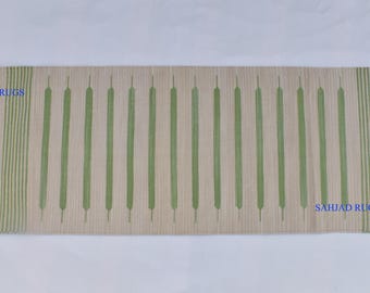 May include: A long, rectangular rug with a cream background and green stripes. The rug has a simple geometric design with vertical lines and a few diamond shapes. The rug is fringed on both ends and has the text "SAHJAD RUGS" printed on the bottom right corner.