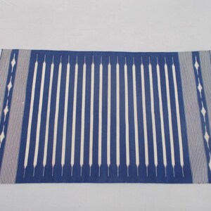 Peut inclure: Un tapis ray&eacute; bleu et blanc avec un motif g&eacute;om&eacute;trique aux extr&eacute;mit&eacute;s. Le tapis est fait d'un mat&eacute;riau tiss&eacute; et a une texture douce.
