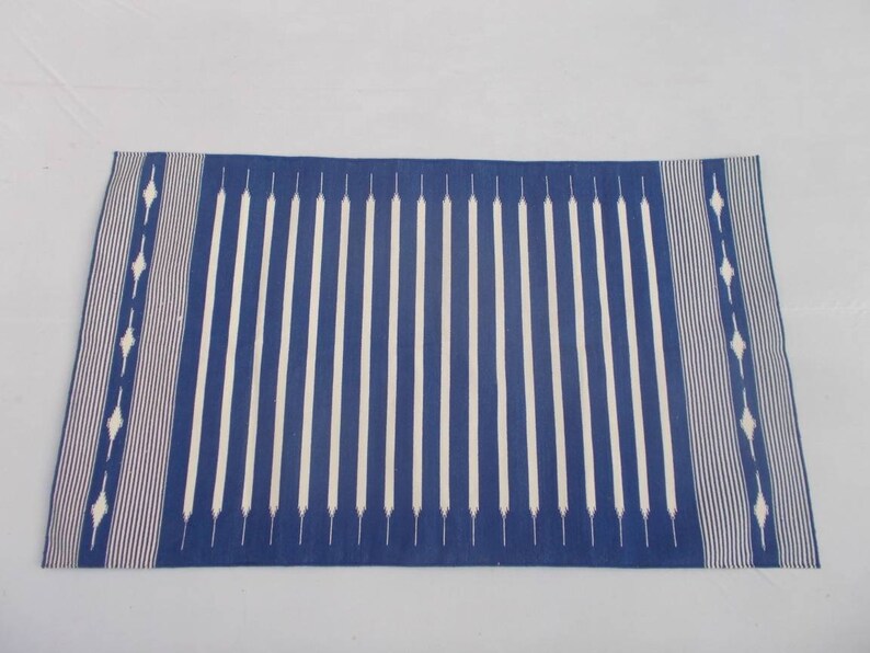 Peut inclure: Un tapis ray&eacute; bleu et blanc avec un motif g&eacute;om&eacute;trique aux extr&eacute;mit&eacute;s. Le tapis est fait d'un mat&eacute;riau tiss&eacute; et a une texture douce.