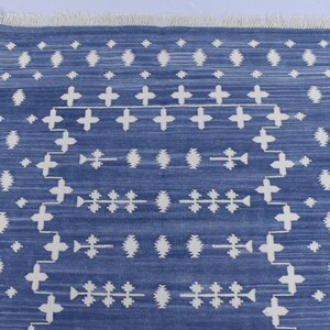 Puede incluir: Una alfombra azul y blanca con un dise&ntilde;o geom&eacute;trico. La alfombra tiene un borde de flecos.