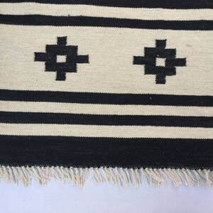 May include: Black and white striped rug with a geometric pattern. The rug has a fringe border.