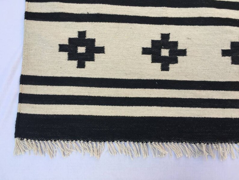 May include: Black and white striped rug with a geometric pattern. The rug has a fringe border.