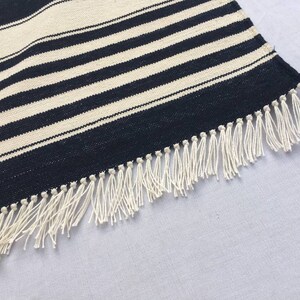 May include: A black and white striped rug with a fringe border. The rug is made of a woven material and has a subtle sheen.