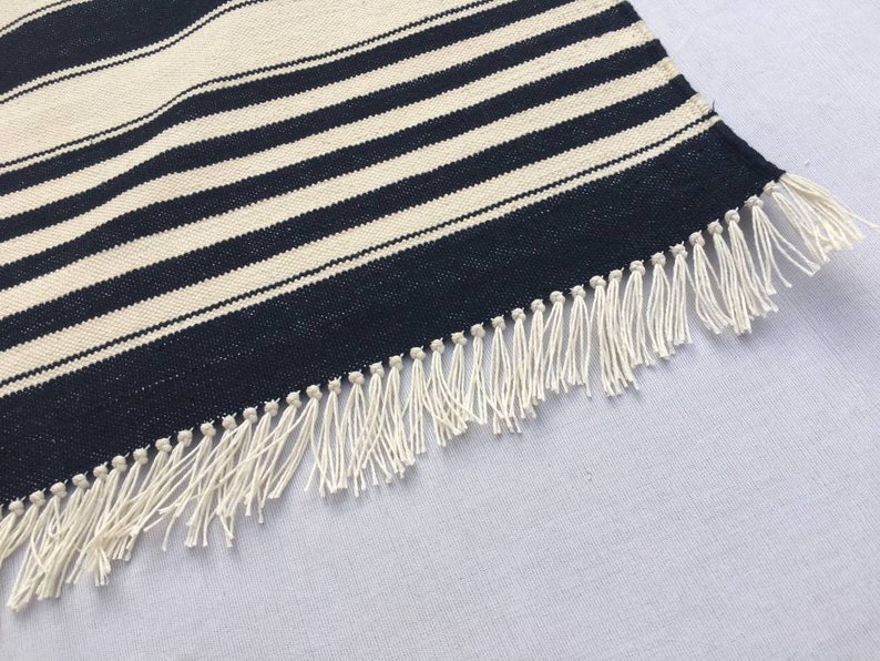 May include: A black and white striped rug with a fringe border. The rug is made of a woven material and has a subtle sheen.