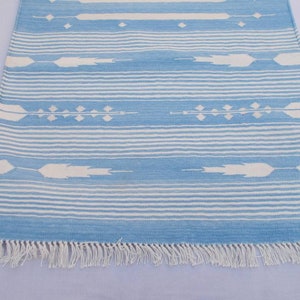 Puede incluir: Una alfombra de rayas azules y blancas con un patr&oacute;n geom&eacute;trico. La alfombra tiene flecos blancos en los bordes.
