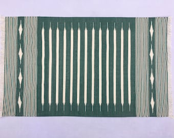 May include: A green and white striped rug with fringe on the ends. The rug has a geometric pattern in the border.