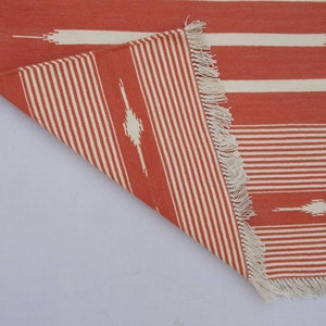 May include: A red and white striped rug with a geometric pattern. The rug has a fringe border.
