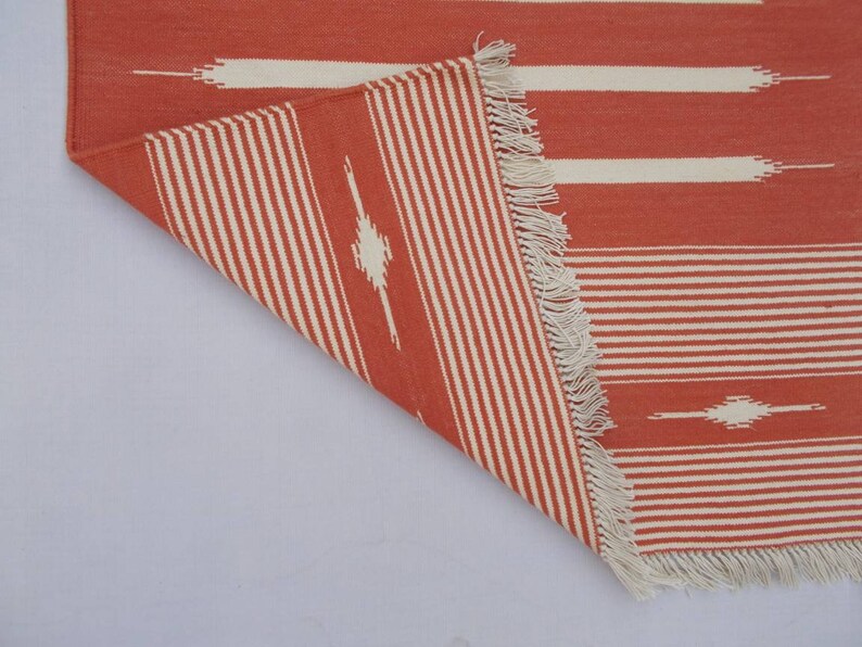 May include: A red and white striped rug with a geometric pattern. The rug has a fringe border.