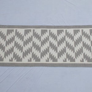 Op de afbeelding: Een grijze en witte geometrisch gepatroneerde loper met franjes.