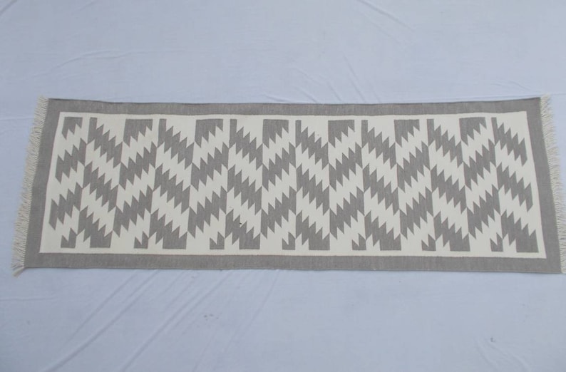 Op de afbeelding: Een grijze en witte geometrisch gepatroneerde loper met franjes.