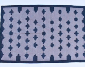May include: A grey and black geometric patterned rug with a fringe border. The rug has a repeating diamond pattern.