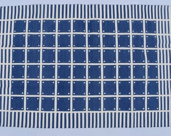 Puede incluir: Una alfombra geométrica azul y blanca con un borde de flecos. La alfombra tiene un patrón de cuadrícula de cuadrados con contornos blancos y puntos blancos en el centro de cada cuadrado. La alfombra tiene un fondo blanco con rayas azules a lo largo de los bordes superior e inferior.
