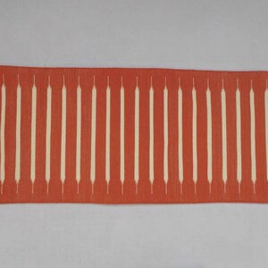 May include: A long, rectangular red runner rug with a white geometric pattern. The rug has fringe on both ends.