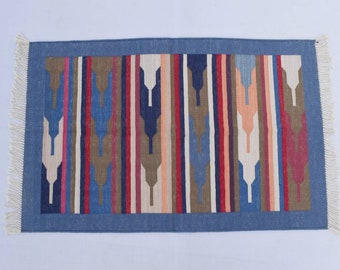 Puede incluir: Una alfombra rayada azul y marrón con un patrón geométrico. La alfombra tiene un borde de flecos y está hecha de algodón.