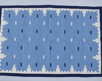 May include: A blue and white patterned rug with a navy blue border. The rug has a geometric design with white and blue rectangles.