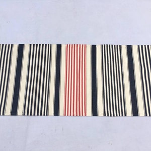 May include: A striped rug with a red stripe in the centre. The rug has a white background with black and navy blue stripes.