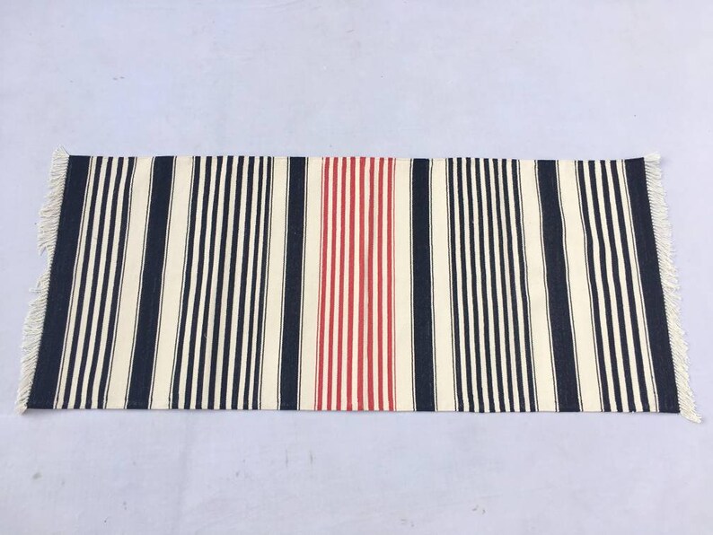 May include: A striped rug with a red stripe in the centre. The rug has a white background with black and navy blue stripes.