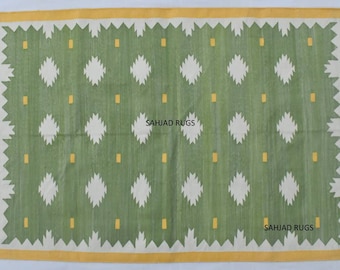 May include: Green and white rug with a geometric pattern and yellow accents. The rug has a fringe border and the text "SAHJAD RUGS" is printed twice on the rug.