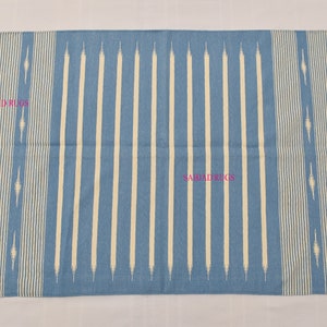 May include: A rectangular blue rug with vertical cream-colored stripes and fringed edges. The rug features a repeating pattern of cream-colored lines and decorative elements. The text "SAHJAD RUGS" is visible on the rug.