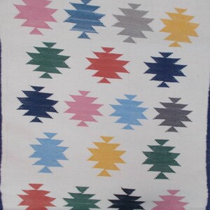 May include: A white rug with a blue border and a pattern of colorful stars. The stars are in shades of pink, blue, green, yellow, and red.