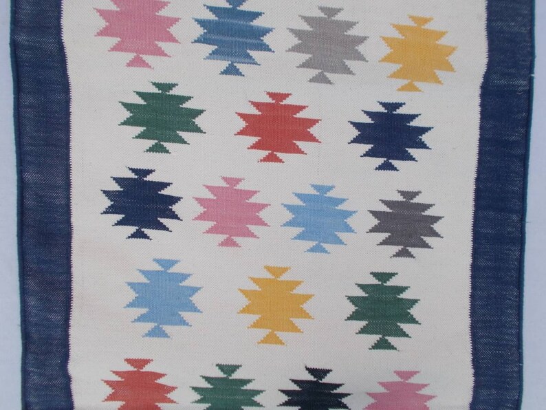 May include: A white rug with a blue border and a pattern of colorful stars. The stars are in shades of pink, blue, green, yellow, and red.