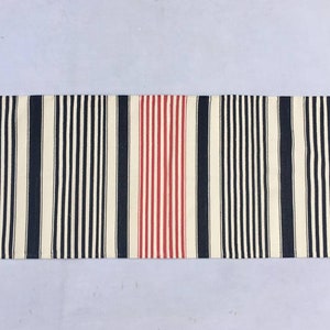 May include: A striped rug with black, white and red stripes. The rug has a fringe on both ends.